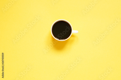 Flat lay cup of black coffee on yellow background. Minimalistic food concept.