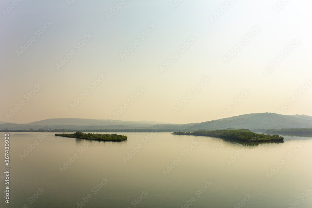 two islands with green forest in a river misty valley under blue sky, aerial view