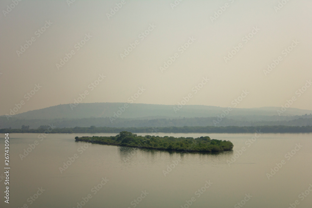small island with bright green trees against the backdrop of a misty river valley