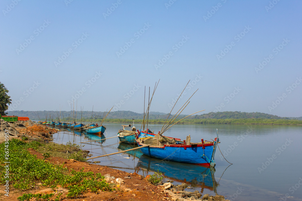 Obraz premium large old fishing boats with motors and fishing rods anchored off the coast against the backdrop of a river and green forest