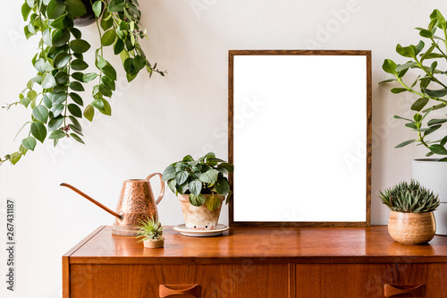Nice and retro space of home interior with mock up poster frame, vintage cupboard with elegant floral accessories, a lot of plants in stylish pots. Cozy home decor. Minimalistic concept. Home garden
