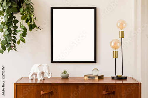 Minimalistic and stylish mock up poster frame concept with retro furnitures, hanging plant, gold table lamp and elegant accessories. White walls, home decor. Nice interior of living room. Real photo. © FollowTheFlow