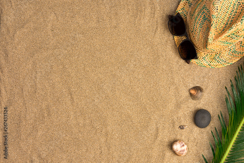 Stylish summer composition with green leaves, hat and sunglasses on a sand background. Artwork mockup with copy space