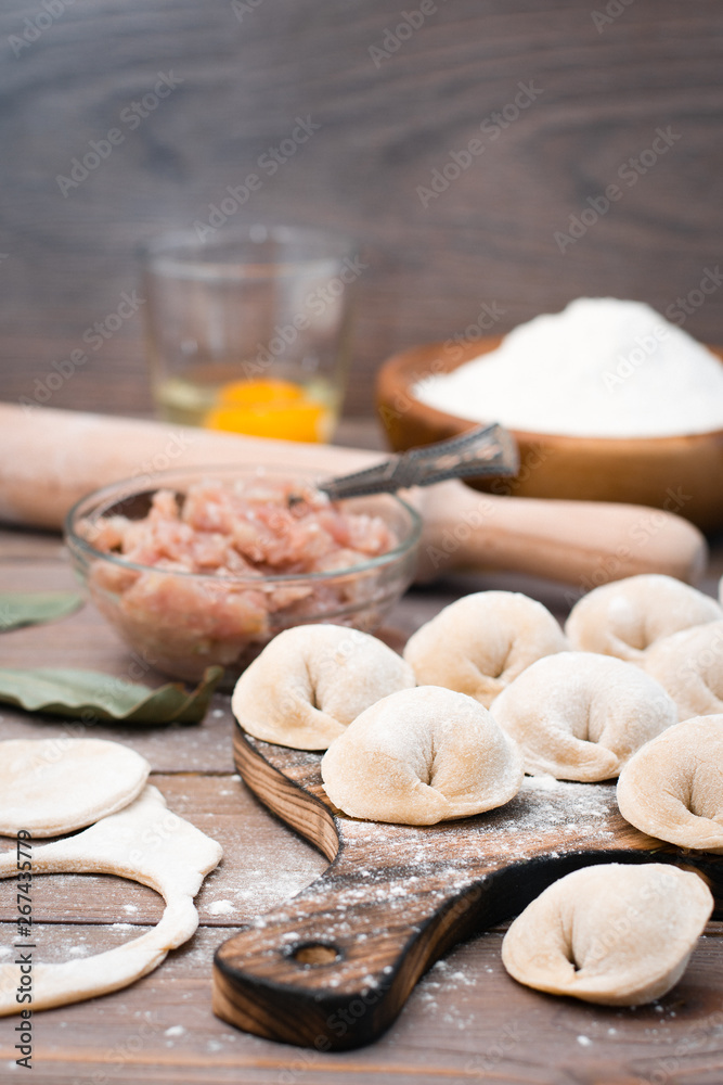 Raw dumplings on the cutting board and ingredients for their preparation: flour, egg, minced meat on a wooden table Raw dumplings on the cutting board and ingredients for their preparation: flour, egg, minced meat on a wooden table