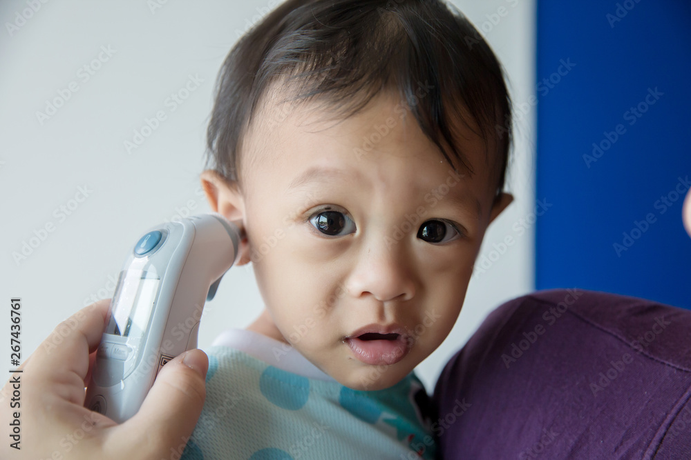 Doctor measuring temperature cute baby boy at hospital . Mother takes temperature for baby boy with ear thermometer at home Doctor measuring temperature cute baby boy at hospital . Mother takes temperature for baby boy with ear thermometer at home