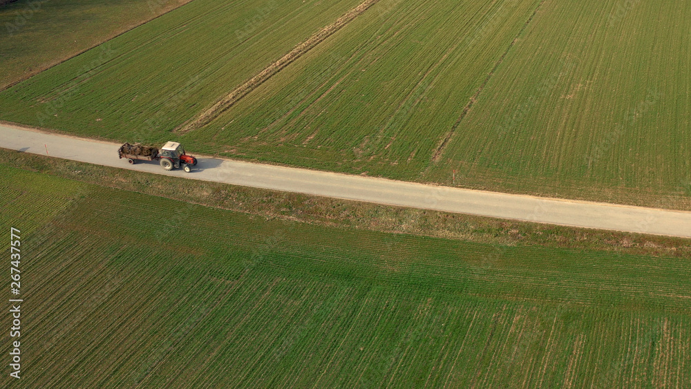 Aerial view of a red tractor and trailer carrying a load of manure on road