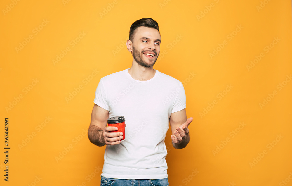 Handsome young man in white t-shirt with cup in hand over yellow background. Handsome young man in white t-shirt with cup in hand over yellow background.