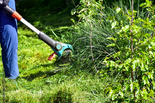 The simple mThoments of life, ordinary work in the garden - man trimming grass with heavy-duty trimmer in the garden, suitable for trimming long lawn edges and larger hard-to-access areas. Man mows .