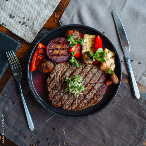 Beef steak with a side dish of grilled vegetables, with natural light from the window on a wooden table, BBQ