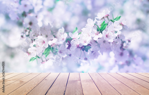 Empty wooden table  natural delicate flowers in the background  sun rays. Light delicate floral background pattern