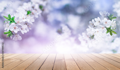 Empty wooden table  natural delicate flowers in the background  sun rays. Light delicate floral background pattern