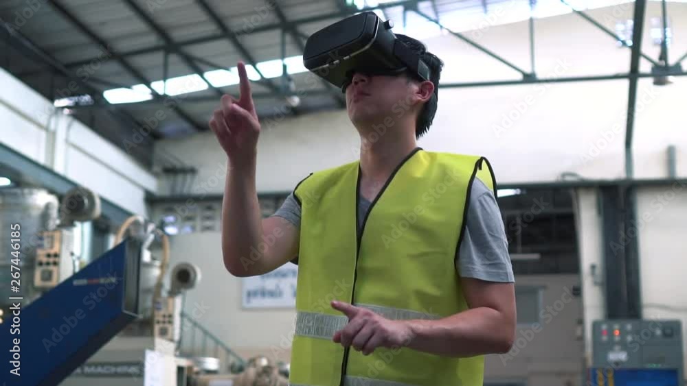 Industrial factory and manfacturing engieering worker wearing VR goggle headset touching in virtual reality simulation alongside heavy duty machines Industrial factory and manfacturing engieering worker wearing VR goggle headset touching in virtual reality simulation alongside heavy duty machines