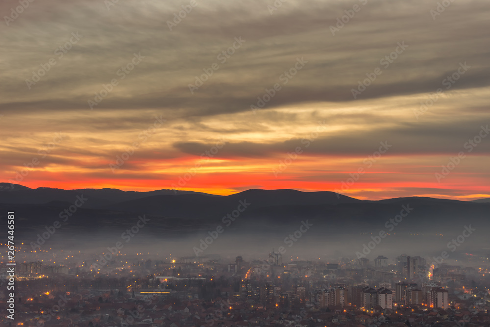 Stunning, soft view of burning sunset sky above scenic cityscape covered by haze and mist
