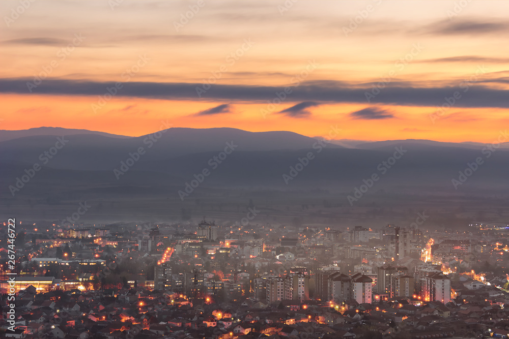 Amazing blue hour sky over Pirot cityscape lighten by city lights and misty horizon mountains