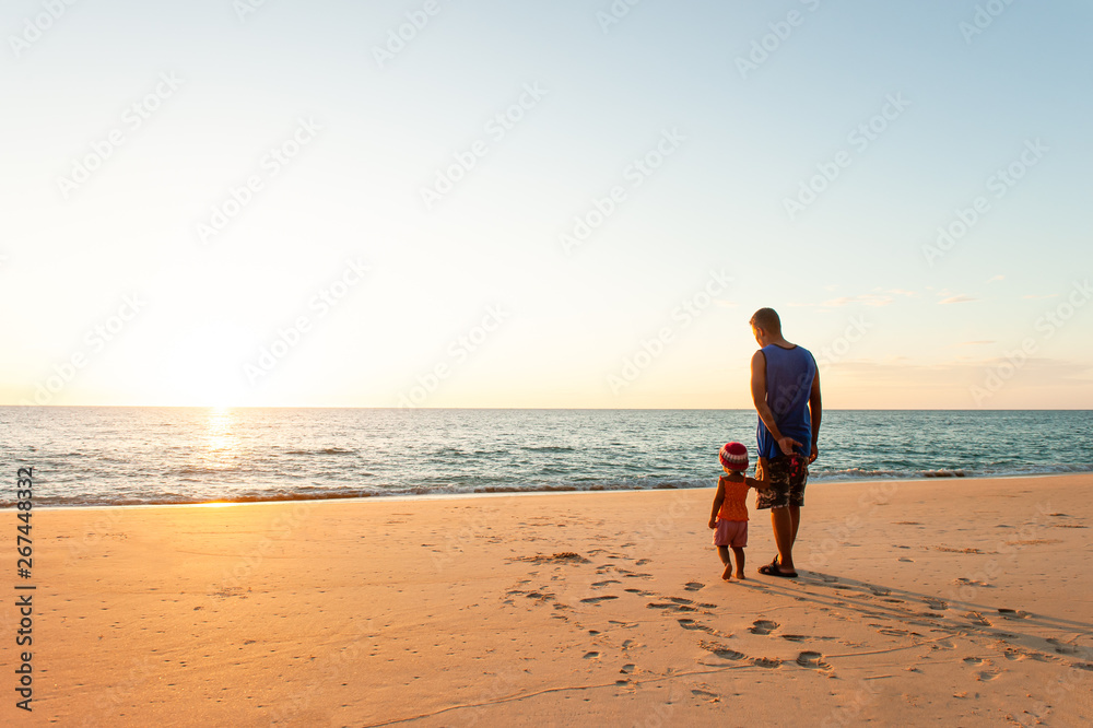 A little girl holding her father hands on the sunset beach.