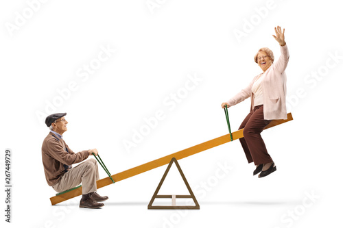 Senior man and woman waving and sitting on a seesaw
