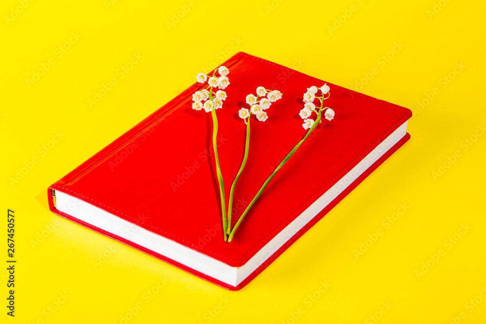 Red notepad with lily of the valley flowers on a yellow background Red notepad with lily of the valley flowers on a yellow background