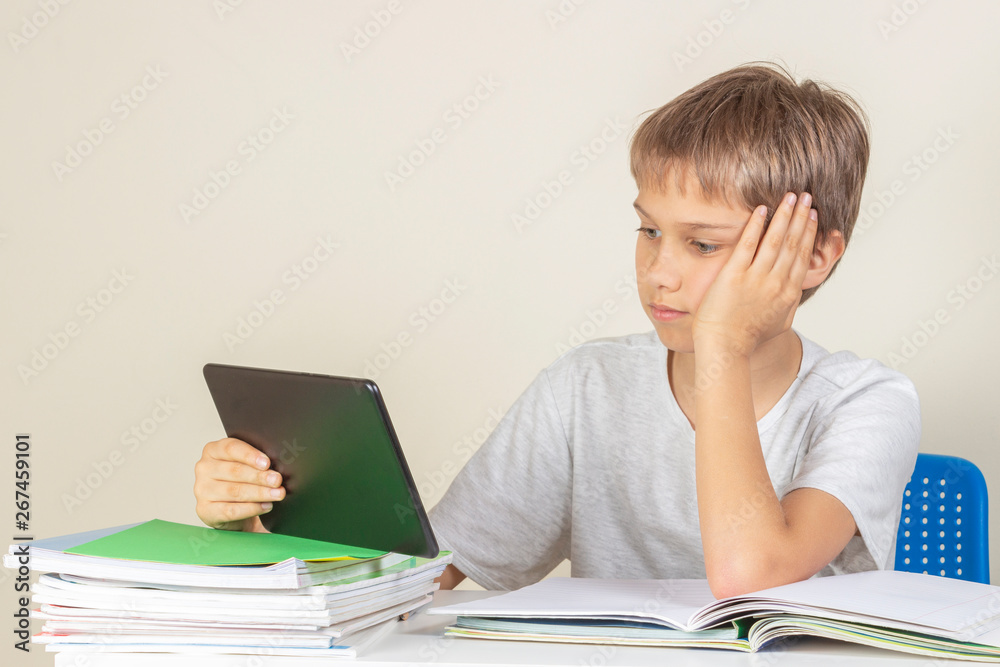 Kid sitting at table with books notebooks and using tablet computer Kid sitting at table with books notebooks and using tablet computer