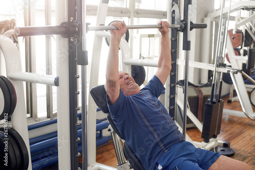 Lying senior man lifting weight at gym. Mature man lifting heavy weight in gym. Weight workout.