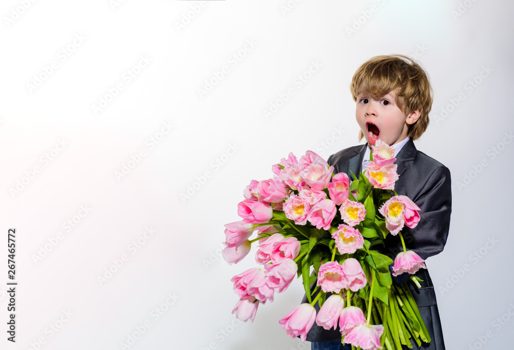 Gift to mum. Surprised little boy with bouquet of tulips. On March 8, International Women's Day, Mother's Day, Valentines day. Wedding concept. Stylish little boy in elegant suit holds bouquet tulips. Gift to mum. Surprised little boy with bouquet of tulips. On March 8, International Women's Day, Mother's Day, Valentines day. Wedding concept. Stylish little boy in elegant suit holds bouquet tulips.