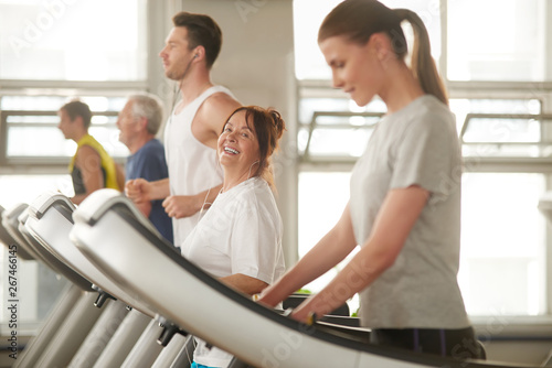Senior woman on treadmill smiling at camera. People exercising at modern sport club. People, fitness, active lifestyle.