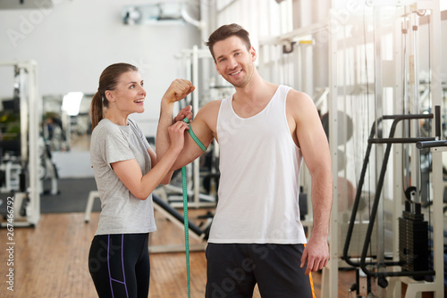 Woman measuring athletics man biceps. Young handsome man showing biceps and looking at camera. Personal sport achievement.