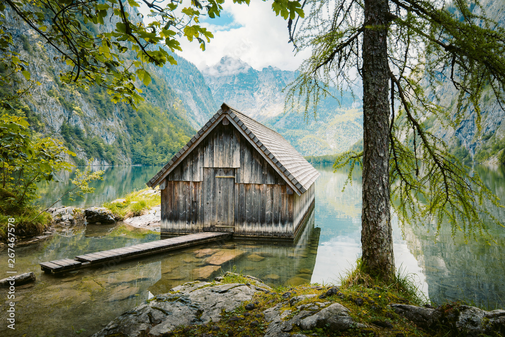 Idyllic view of traditional old wooden boat house at scenic Lake Obersee on a beautiful sunny day with blue sky and clouds in summer, Nationalpark Berchtesgadener Land, Bavaria, Germany