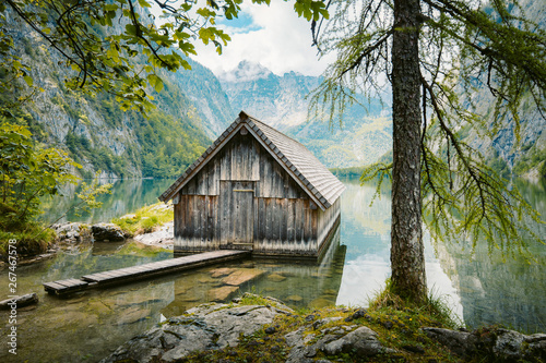 Obraz na płótnie Idyllic view of traditional old wooden boat house at scenic Lake Obersee on a beautiful sunny day with blue sky and clouds in summer, Nationalpark Berchtesgadener Land, Bavaria, Germany w salonie