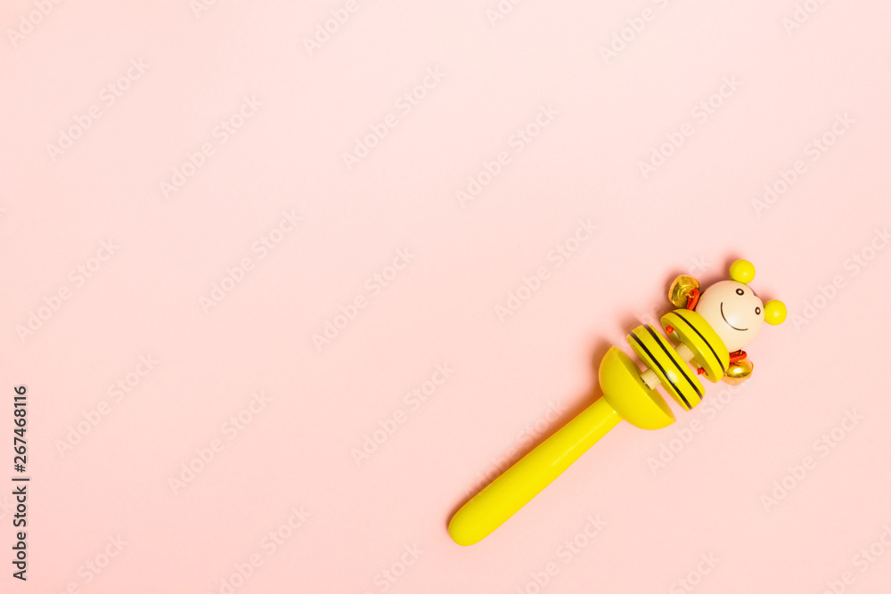 Baby wooden rattle with metal bells for small child. Yellow toy on pink background with copy space. Flat lay style Baby wooden rattle with metal bells for small child. Yellow toy on pink background with copy space. Flat lay style