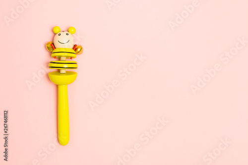 Yellow wooden baby toy with bells. Traditional rattle on pink background. Overhead view. Copy space. Flat lay style
