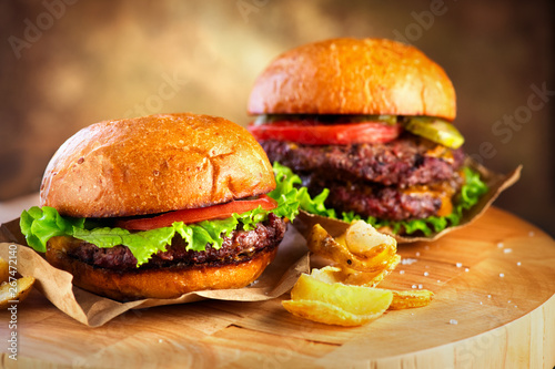 Hamburger and Double Cheeseburger with fries wooden table background. Cheeseburgers on fresh buns with succulent beef and fresh salad ingredients served with french fries