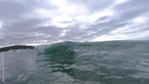 wave in calm ocean peeling and tubing towards camera as backwash causes tube to lurch and undulate several times towards camera.  dark and stormy skies and slow motion add drama.