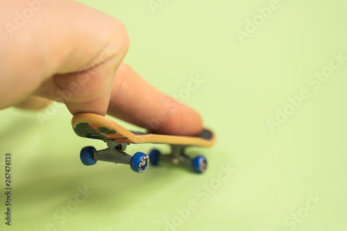 Fingerboard. Man make trick by two fingers with small skateboard on green background. photo