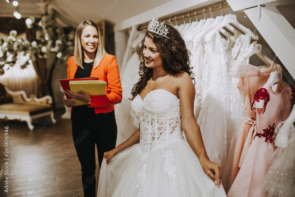 Naklejka premium Beautiful young brunette woman choosing wedding dress in a bridal salon.