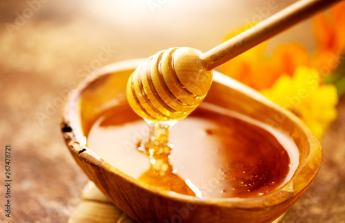 Honey dripping from honey dipper in wooden bowl. Healthy organic thick honey pouring from the wooden honey spoon closeup