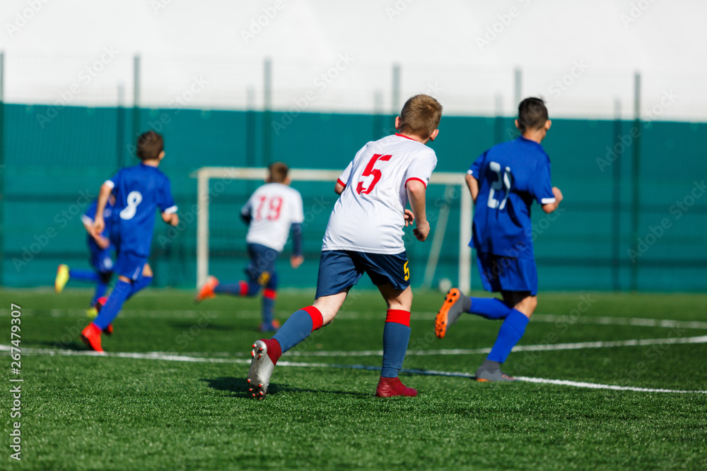 Junior football match. Boys in blue white sportswear play soccer match on football pitch. Football stadium, grass field at the background Soccer for young players. Training, sport, activity outdoor Junior football match. Boys in blue white sportswear play soccer match on football pitch. Football stadium, grass field at the background Soccer for young players. Training, sport, activity outdoor