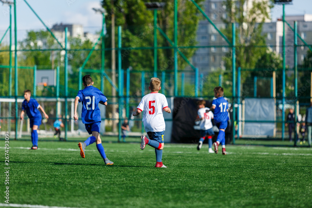 Junior football match. Boys in blue white sportswear play soccer match on football pitch. Football stadium, grass field at the background Soccer for young players. Training, sport, activity outdoor Junior football match. Boys in blue white sportswear play soccer match on football pitch. Football stadium, grass field at the background Soccer for young players. Training, sport, activity outdoor