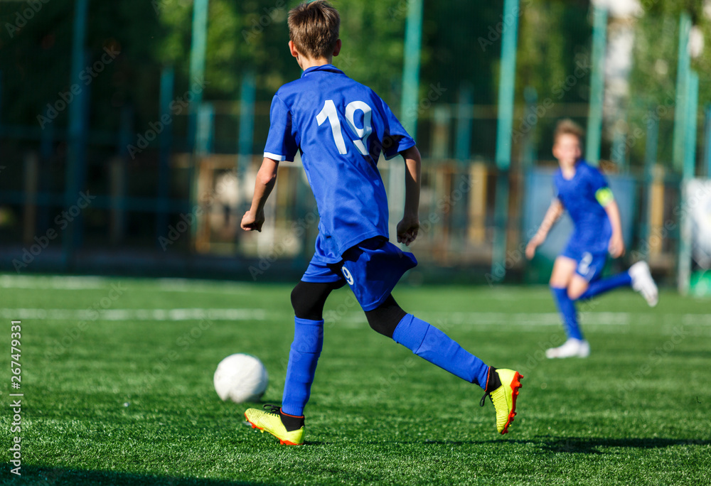 Junior football match. Boys in blue white sportswear play soccer match on football pitch. Football stadium, grass field at the background Soccer for young players. Training, sport, activity outdoor