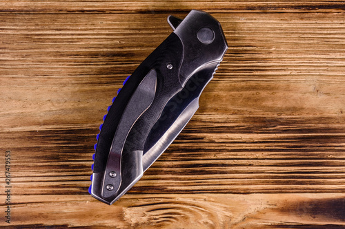 Closed folding knife on a wooden table. Top view