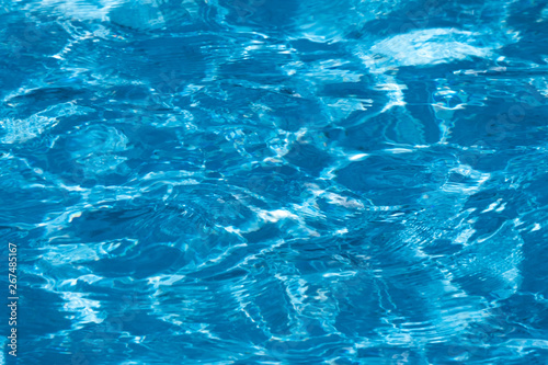Blue and bright ripple water surface in swimming pool with sun reflection. © pookpiik