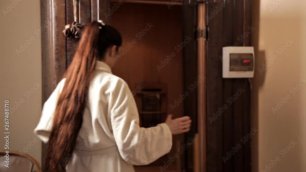 A young girl in a white robe opened the glass door and entered the sauna A young girl in a white robe opened the glass door and entered the sauna