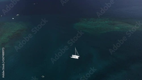 HIGHT angle shot, Top view of the boat. Aerial View of a Anchored Catamaran Yacht Standing and people can Sunbathing on it's Deck. Runabout or cruiser stands in azure Sea Waters With Coral Reef photo