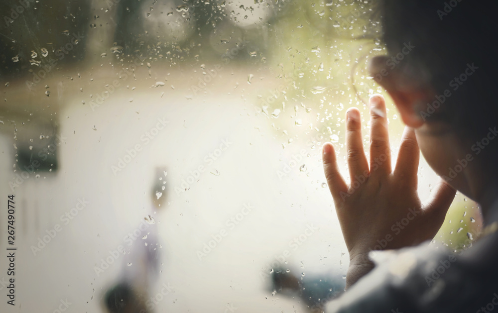Little girl  by window with raindrops on it on a rainy day