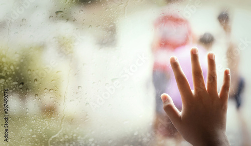 Hand of little girl  by window with raindrops on it on a rainy day.