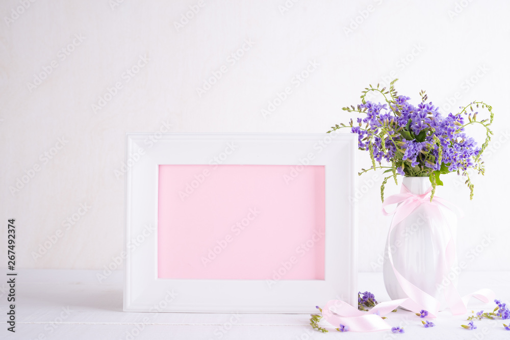 White picture frame with lovely purple flower in vase on white wooden table. White picture frame with lovely purple flower in vase on white wooden table.