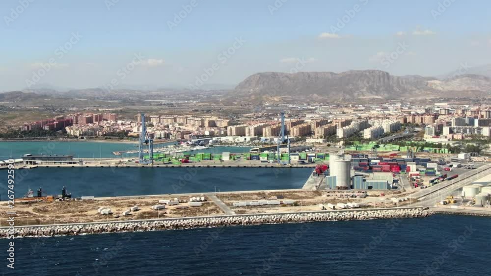 Slow motion view from drone flying in from the sea toward the port of Alicante, Spain. Brown dry landscape and tall buildings of the city in the distance. Shipping industry in Europe. Aerial view. Slow motion view from drone flying in from the sea toward the port of Alicante, Spain. Brown dry landscape and tall buildings of the city in the distance. Shipping industry in Europe. Aerial view.