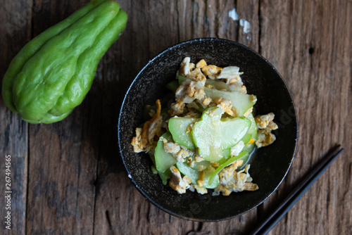 Fresh chayote fruits (Sechium edulis) stir fried with egg and garlic in bowl on wood background