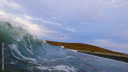 Wave backwash causes unexpected huge round tubular splash over camera.  5x slow motion shot at 120 frames per second and cloudy stormy skies add to the drama.