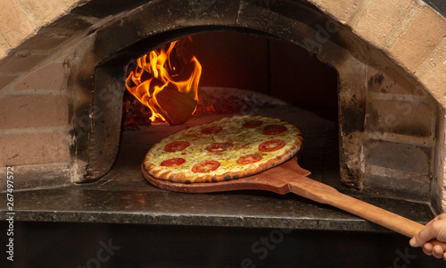 Brazilian pizza is cooked in a wood-fired oven. Pizza cooking in a traditional brick wood oven. Brick oven pizza on the wooden holder going to bake.