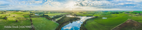 Wide aerial panorama of river flowing through grasslands, meadows, and pastures in Australia at sunset